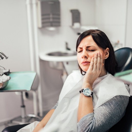 Woman sitting in dental chair and holding her cheek in pain